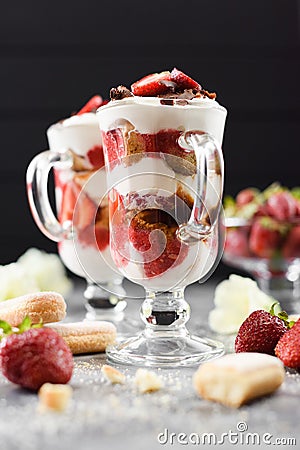 Comfort food. Italian dessert tiramisu with raw strawberries in Irish glasses on dark background side view Stock Photo