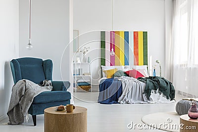 Comfortable armchair with grey blanket in colorful bedroom with king size bed and multicolored headboard Stock Photo