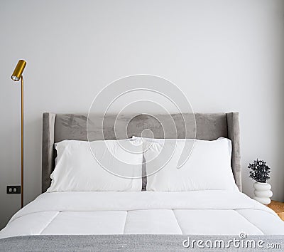 Comfortable bed in modern bedroom, pillows and white soft blanket on bed, lamp and vase decorate in room. Free white wall space Stock Photo