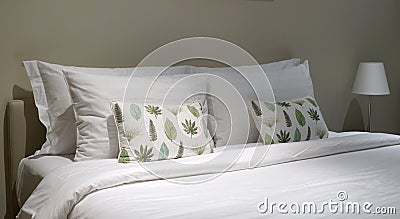 Comfortable throw cushion on the white pillow s and white bedsheet with three hanging picture frames Stock Photo