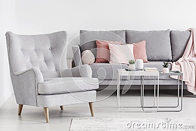 Comfy armchair and grey sofa with pink pillows, and coffee table Stock Photo