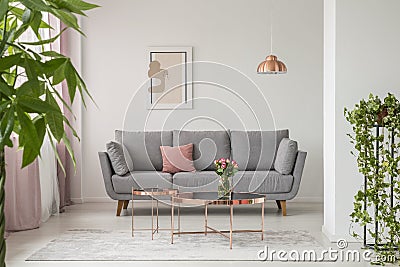 Comfy sofa, copper coffee table and plants in a bright living room interior Stock Photo