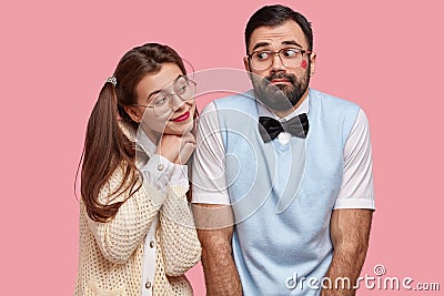 Comic young woman with two pony tails looks with love at boyfriend who has red lipstick on cheek after recieving kiss Stock Photo