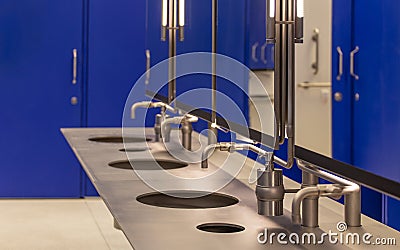 Commercial bathroom for hand washing. Faucets with a washbasin in a public toilet are blue. Stock Photo