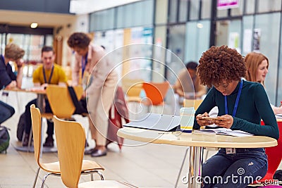 Communal Area Of Busy College Campus With Female Student Working At Tables And Using Mobile Phone Stock Photo