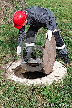 The communal worker opened the sewer hatch and looks inside. Inspection and maintenance of water wells and sewer wells Stock Photo