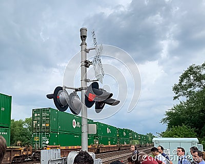 Commuters wait for a freight train to pass through Villa Park, IL at the railroad crossing above ground Editorial Stock Photo
