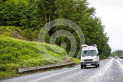 Compact cargo mini van with tubes on the roof running to side of the service driving on the wet highway road at rainy weather Stock Photo