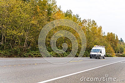 Compact mini van with leaders on the roof driving on autumn road with yellow trees Stock Photo