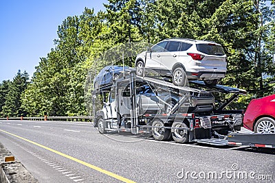 Compact powerful white big rig car hauler semi truck transporting cars on two hydraulic modular semi trailer running on the wide Stock Photo