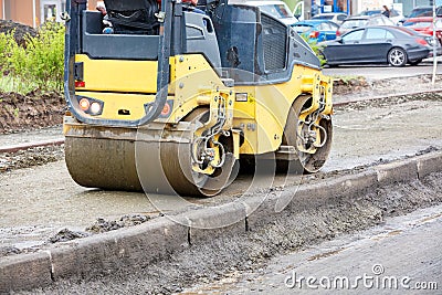 The compact road roller ramps the pavement foundation along the concrete curb and driveway Stock Photo