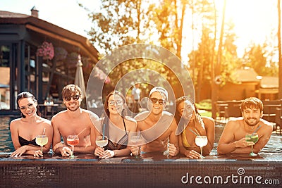 Company of happy friends drinks cocktail drinks in pool at summertime. Swimming pool party. Stock Photo