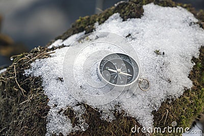 The compass is lying on the snow on the lake shore . The arrow points to the North Stock Photo