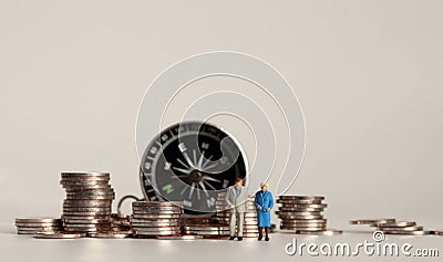 Compass and pile of coins. A miniature old couple. Stock Photo