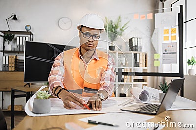 Competent arhitect male sitting on desk indoors using pen and ruler for project drawings. Stock Photo
