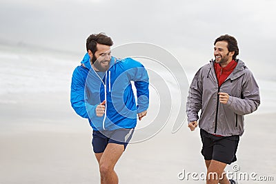 Competing with a Friend. two young men jogging together along the beach on an overcast morning. Stock Photo