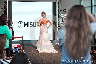Competition of wedding stylists. A model in a white wedding dress with an open back and with a hairdo walks along the Editorial Stock Photo