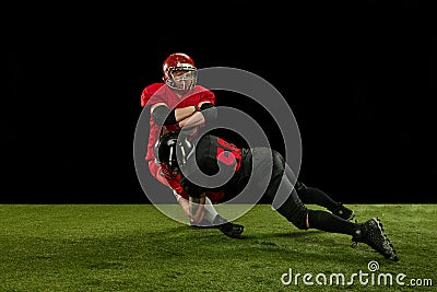 Competitive spirit. Two men, american football players in full uniform and equipment on field playing over black Stock Photo