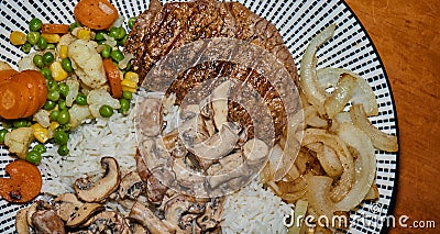Complete meal of a grilled pork steak with roasted onions, vegetable mix of peas, carrots, corn and cauliflower, on rice with Stock Photo