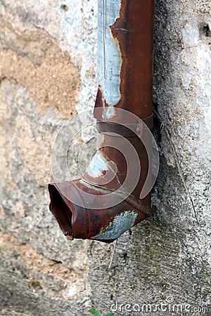 Almost completely rusted and beaten down gutter rainfall exit mounted with metal brackets on side of dilapidated cracked family Stock Photo