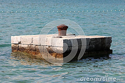 Completely rusted dilapidated iron mooring bollard in middle of stone pier surrounded with calm sea used for tying larger ships Stock Photo