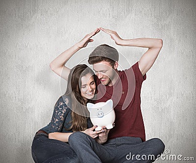 Composite image of couple sitting on floor with piggy bank Stock Photo