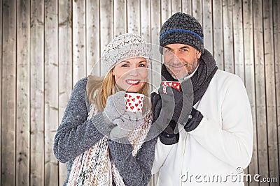 Composite image of happy couple in winter fashion holding mugs Stock Photo