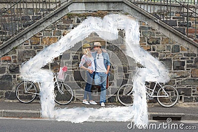 Composite image of hip young couple standing by brick wall with their bikes Stock Photo