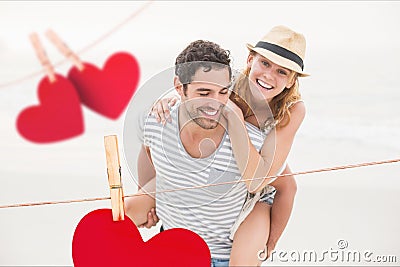 Composite image of red hanging hearts and man giving piggyback to woman Stock Photo
