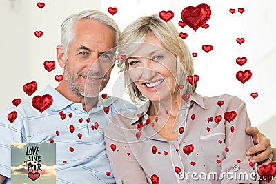 Composite image of smiling mature couple sitting on sofa with arm around Stock Photo