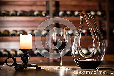 Composition of carafe, glass with wine and canddle. Shelves with wine bottles on a background. Stock Photo