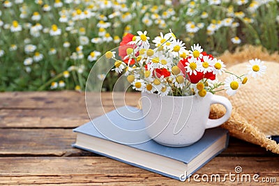 Composition with chamomiles, poppies, straw hat and book on table outdoors Stock Photo