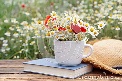 Composition with chamomiles, poppies, straw hat and book on table outdoors Stock Photo