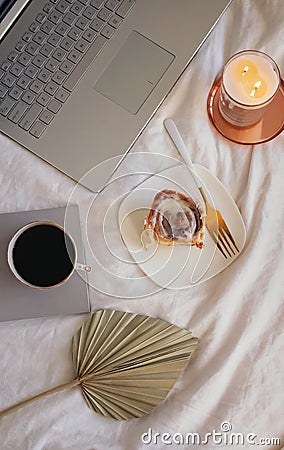 Composition with cinnamon bun, coffee, burning candle and laptop on the bed. Stock Photo