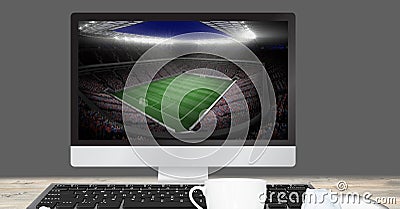 Composition of desk and cup of coffee over football stadium in computer Stock Photo