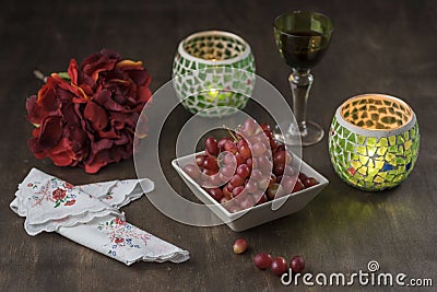 Composition with grape, candlesticks, a wine glass, decorative peony flower, and embroidered napkins Stock Photo