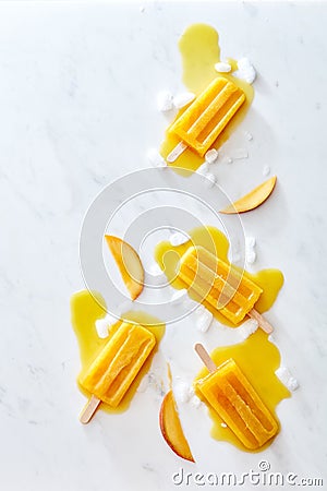 Composition of juicy pieces of peach, ice and melting ice cream on a stick with splashes on a gray marble table with Stock Photo