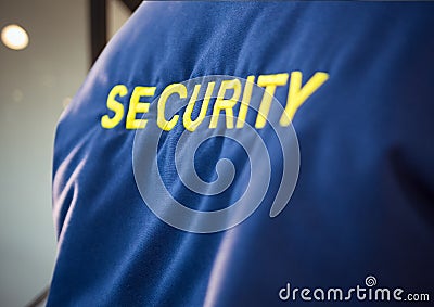 Composition of midsection of security guard blue jacket with yellow text over blurred background Stock Photo