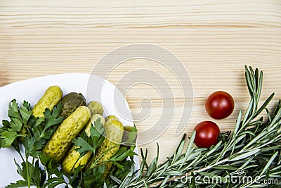 Composition with pickled cucumbers on the white plate with tomatoes, rosemary and parsley on wooden background. Cooking food Stock Photo