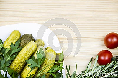 Composition with pickled cucumbers on the white plate with tomatoes, rosemary and parsley on wooden background. Cooking food Stock Photo