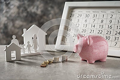 Composition with piggy bank, calendar and model of house and family on grey table. Concept of saving money for buying new house Stock Photo