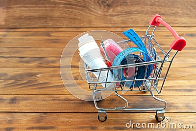 Tailor needles, threads, seam ripper and measuring tape in a shopping cart with wooden background. Cost sewing supplies. Stock Photo