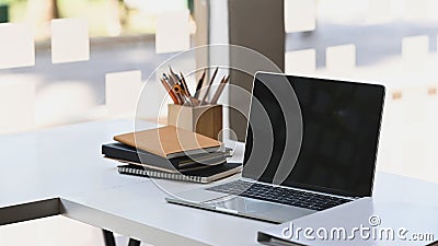 Computer laptop with blank black screen putting on the modern working table with wooden pencil holder, stack of books. Stock Photo