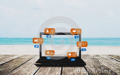Computer laptop on wooden table at the beach in summer, with social media, social network notification icons Stock Photo