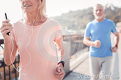 Concentrated aged woman running and holding the smartphone. Stock Photo