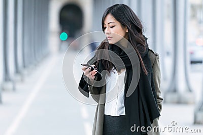Concentrated asian young woman using her mobile phone in the street. Stock Photo