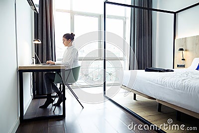 Concentrated beautiful businesswoman working with her laptop on the desk at the hotel room Stock Photo