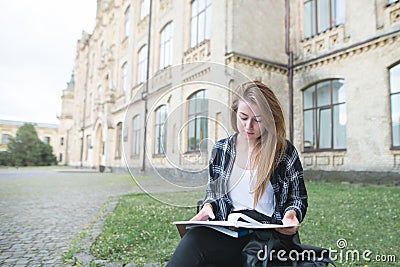 Concentrated beautiful girl student sitting on a bench on college campus and reading Stock Photo