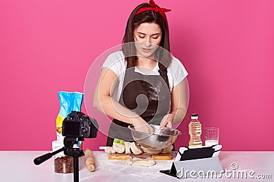 Concentrated busy talented housewife holding bowl with whisk in one hand, being focused on preparation, making culinary Stock Photo