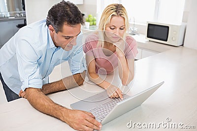 Concentrated couple using laptop in kitchen Stock Photo